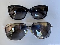 Top view of two pairs of sunglasses: black cat-eye frame and aviator style metal frame