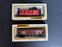 Two Bachmann HO scale train cars in original boxes showing red caboose and brown covered hopper car with Canadian National markings.