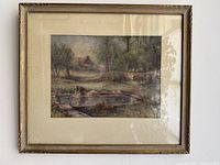 Framed watercolor landscape painting with visible reflections on glass, showing a rural scene with trees, a pond or wash area with a person, and distant structures.
