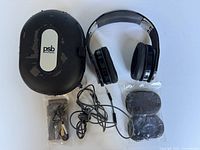 Overhead image of headphones, case, coiled cables and sealed pack of extra ear pads arranged on white surface.