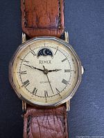 Close-up view of the watch face showing brand name Remex, moonphase complication at 12 o'clock, Roman numerals and ornate watch hands.