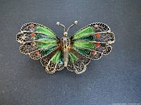 Front view of the vintage silver filigree and enamel butterfly brooch on a dark background showing intricate filigree and enamel decoration.