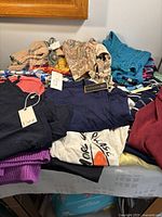 Photo showing assorted ladies summer tops and tanks folded in a pile, including knit, printed and solid colors such as navy, teal, burgundy, and purple with visible brand tags Dex and Harley Davidson.