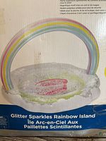 Close-up of the clear inflatable pool float with embedded glitter sparkles and rainbow arch showing the product name on the box.