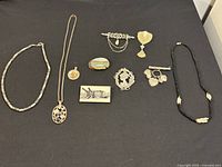 Full view of 10 costume jewelry pieces laid on black background: 3 necklaces, 6 brooches, 1 pendant.