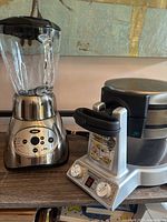Side-by-side photo of Oster 18 speed blender and Cuisinart Breakfast Central waffle and omelette maker on a wooden surface.
