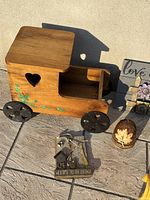 Wooden vintage truck planter with floral details and black metal wheels, small garden signs, and other decorative items arranged on concrete surface