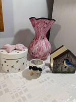 Photo of all four items: pink glass vase, birdhouse napkin holder, round trinket box with bow lid, and sheep figurine.