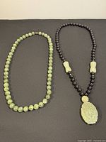 Two necklaces displayed side by side on a surface showing green jade bead necklace and black onyx necklace with jade accents and pendant.