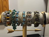 Eight assorted ladies bracelets displayed on a beige bracelet holder. Varied styles with colorful beads, silver-tone metals, and decorative stones.
