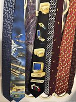 Eight assorted neckties laid out flat, showing patterns and colors including novelty and silk ties, with a variety of themes such as aviation, technology, geometric shapes, and animals.