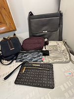 Six handbags and pouches displayed on table including Roots crossbody, XOXO shoulder bag, Athleta pouch, My Tagalongs pouch, Rampage wristlet, and Day2day pouch.