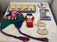 Photo showing all items arranged on a white patterned surface including the Winnie the Pooh tray set with removable dishes, Peppa Pig hat, red soldier mittens, airplane plush, crayons box, and baby sleeping sign.