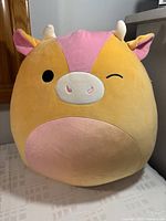 Front view of the Adjani the Sunset Cow Squishmallow plush, showing round body and winking expression.