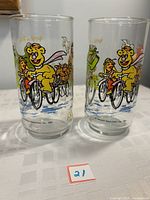 Two clear collectible glasses showing colorful artwork of Muppet characters riding bicycles with McDonald's logo on base.