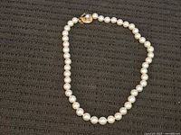 Full view of pearl necklace laid out showing uniform round white pearls and gold clasp.