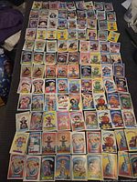 Top-down view of a large assortment of Garbage Pail Kids cards arranged on the floor, displaying various characters and designs.