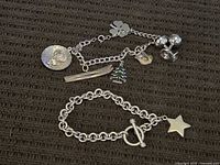 Two sterling silver charm bracelets displayed on a fabric surface showing overall condition and charms.