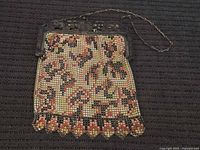 Antique metal mesh purse laid flat displaying its floral pattern and scalloped bottom edge with attached chain handle