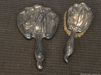 Photo of the full set showing the hand mirror and matching brush with embossed metal backs featuring an Art Deco lady and rose motif.