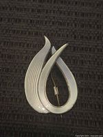 Front view of the brooch showing the white enamel and silver teardrop design on a black textured background.