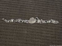 Full view of the sterling silver bracelet laid flat on a textured dark fabric background, showing all animal charms and the ark in the center.