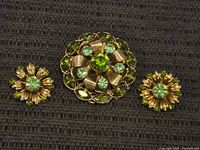 Front view of vintage rhinestone jewelry set showing brooch and matching earrings with green stones on dark fabric