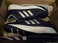 Side view of the navy blue adidas sneaker inside original box showing white stripes and sole.