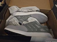 Side view of gray Adidas sneakers in box with tissue paper, showing outsole and Cloudfoam midsole