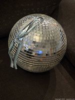 Full size disco ball resting on dark fabric surface showing square mirror tile coverage and attached hanging strap.
