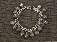 Top-down view of the sterling silver jingle bracelet laid flat on a textured black surface, showing all 15 bells and clasp.