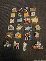 Flat lay showing all 24 assorted colorful Disney enamel pins on a gray surface.