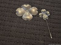 Top view of a matching sterling silver flower brooch and stick pin displayed on a dark textured surface