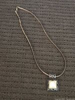 Full view of the silver snake chain necklace with pendant laid flat on a textured surface.