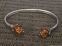 Photo of the open sterling silver bangle bracelet showing the amber stones at each end on a dark textured surface.