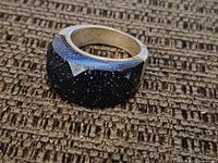 Photo of chunky sterling silver ring with large dark blue glittery cabochon stone showing front and side angle on brown textured surface.