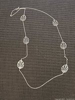 Full length of sterling silver leaf necklace laid flat with six spaced leaf pendants.