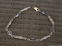 Full length view of the sterling silver bracelet showing the alternation of silver and amethyst-colored stones laid flat.