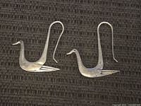 Pair of sterling silver duck-shaped earrings laid flat on a textured black surface.