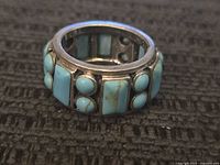 Close-up front view of sterling silver ring with turquoise inlays, showing rectangular and round turquoise pieces set in silver band.