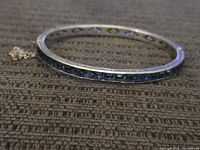 Side angle showing the sterling silver bracelet with inlaid blue oval stones and engraved detailing on band.