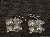 Pair of sterling silver bunny earrings placed side by side on a dark textured background, showing their shape and details.