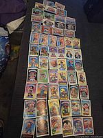 Photo showing a large assortment of Garbage Pail Kids cards laid out in rows on a surface.
