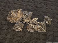 Front and angled view of the vintage silver filigree flower brooch showing detailed filigree flower, leaves, and bud on textured background.