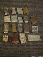 Overhead view of 18 assorted metal and leather vesta cases on fabric