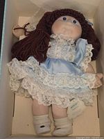 Full body image of the porcelain Cabbage Patch doll in blue satin and white lace dress inside the box