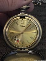 Front face of the vintage Disney pocket watch showing Mickey Mouse design with Roman numerals and gold-toned dial.