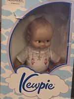 Front view of Kewpie doll in original box with visible blue sky and cloud design.