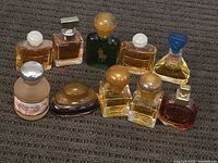 Nine assorted vintage miniature sample perfume bottles on fabric surface, showing variety in bottle shapes, cap styles, and liquid colors