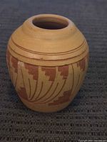 Full view of a small Navajo pottery vase showcasing geometric patterns in brown on a light brown base with a narrow neck and wide body.